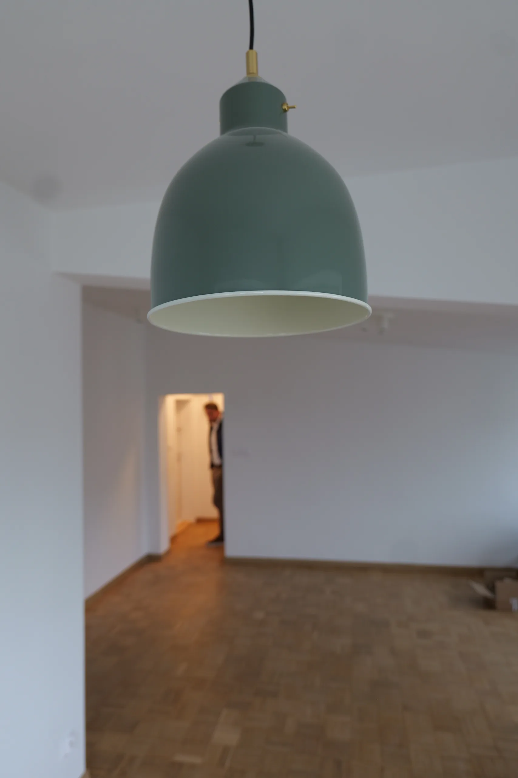Detal wnętrza: turkusowa lampa wisząca w kształcie klosza, w tle rozmyty korytarz z odsłoniętą czerwoną cegłą na ścianie